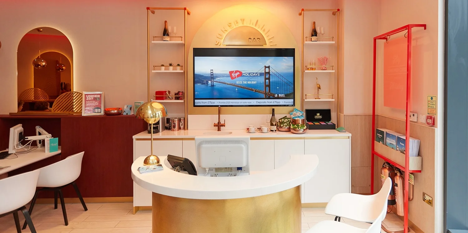 Virgin Holidays Vroom Chelmsford store with a curved reception desk a large TV screen shelving and a red brochure rack